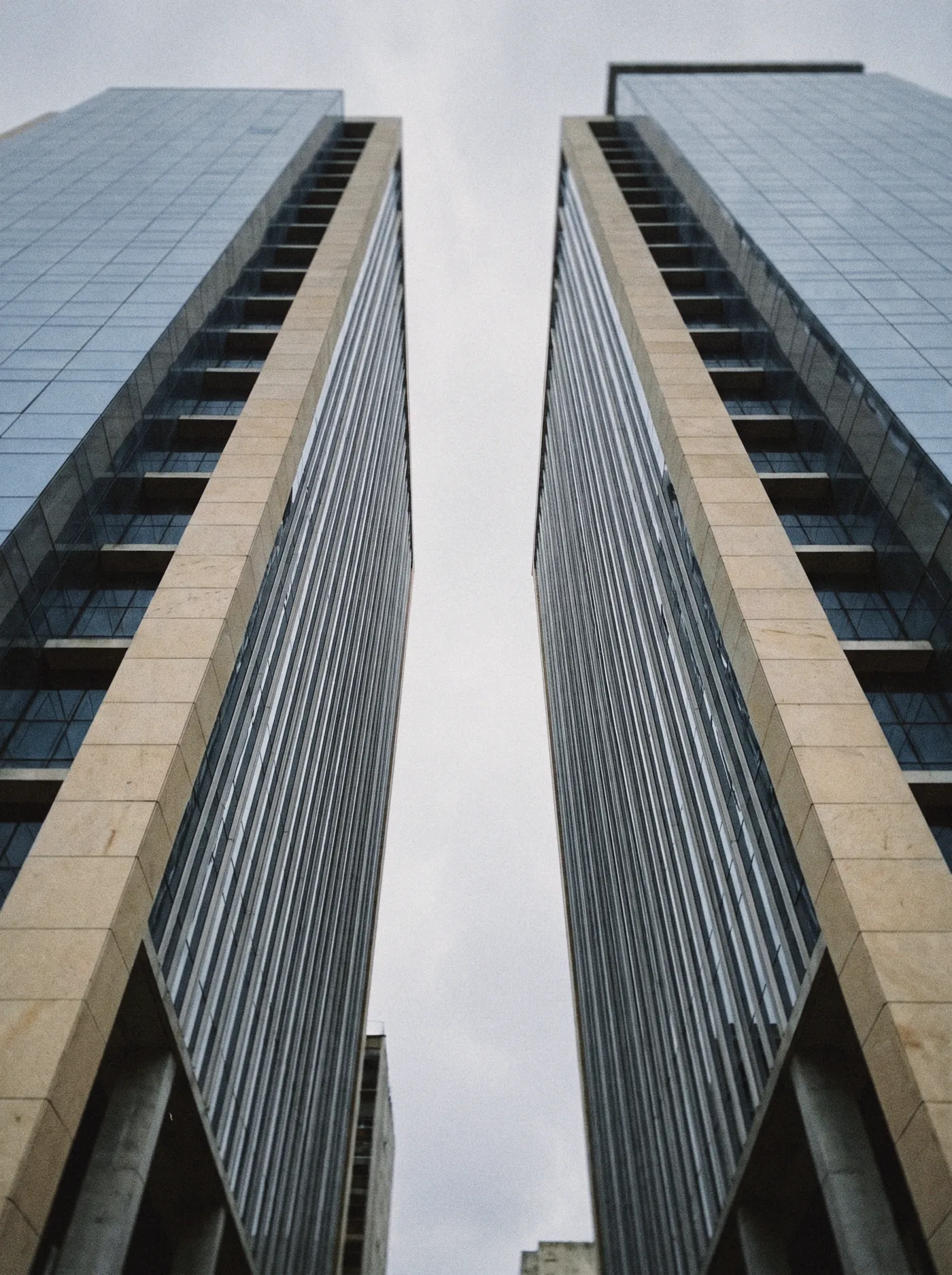 Duas torres corporativas de pedra e vidro vistas de baixo, subindo em direção ao céu
